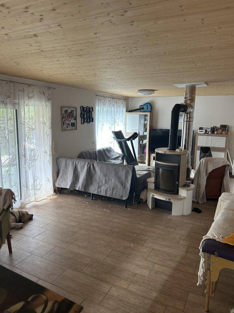 Geräumiges Wohnzimmer mit Holzbalkendecke, Fliesenboden und einem gemütlichen Holzofen.