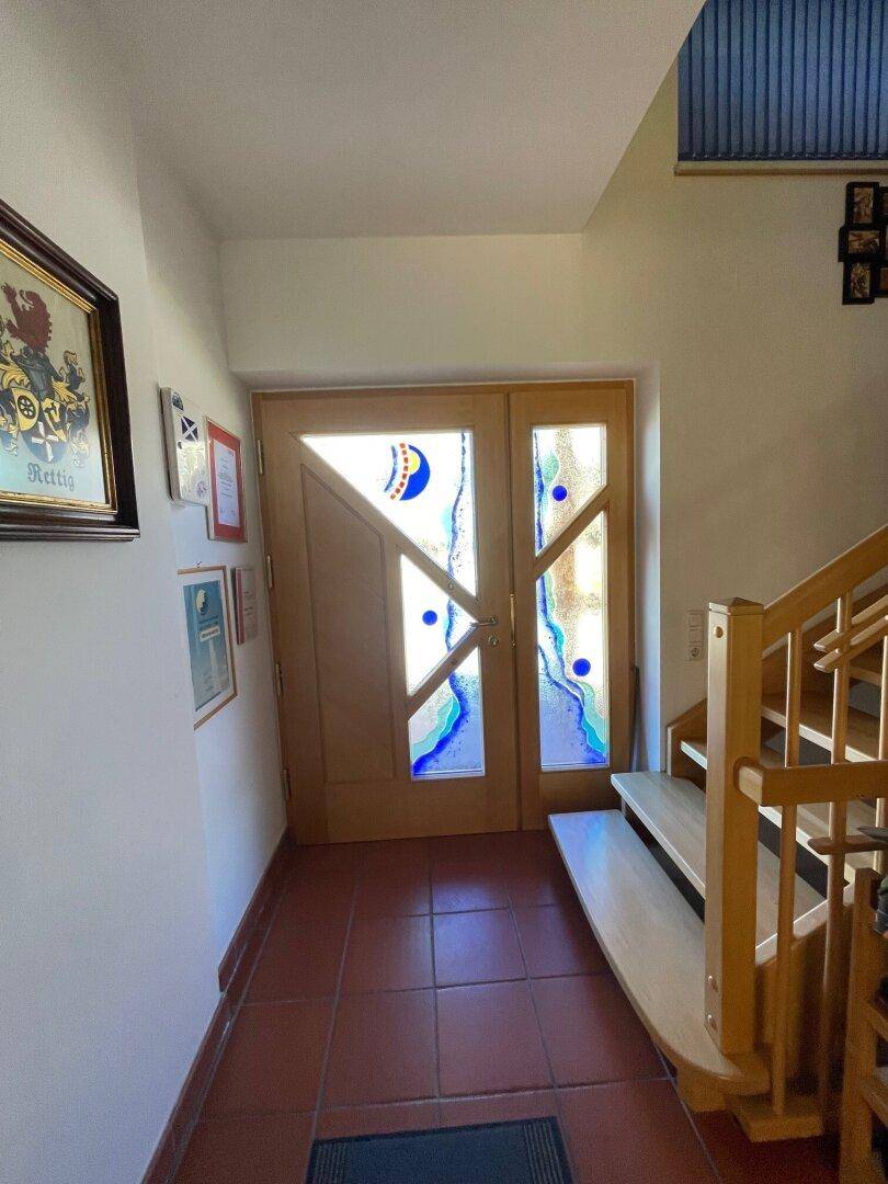 Heller Eingangsbereich mit Holztür, Buntglasfenstern und Holztreppe zum Obergeschoss.