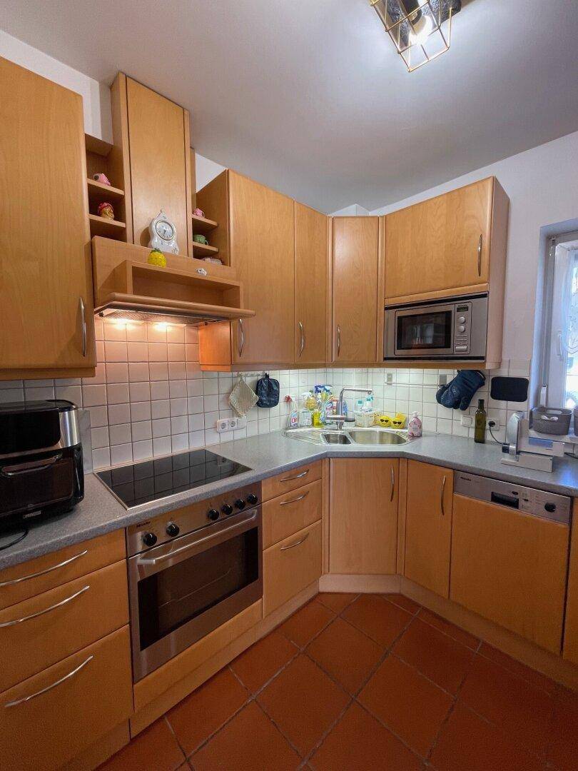 Funktionale Küche mit Holzschränken, Einbaugeräten und Terrakotta-Fliesenboden.