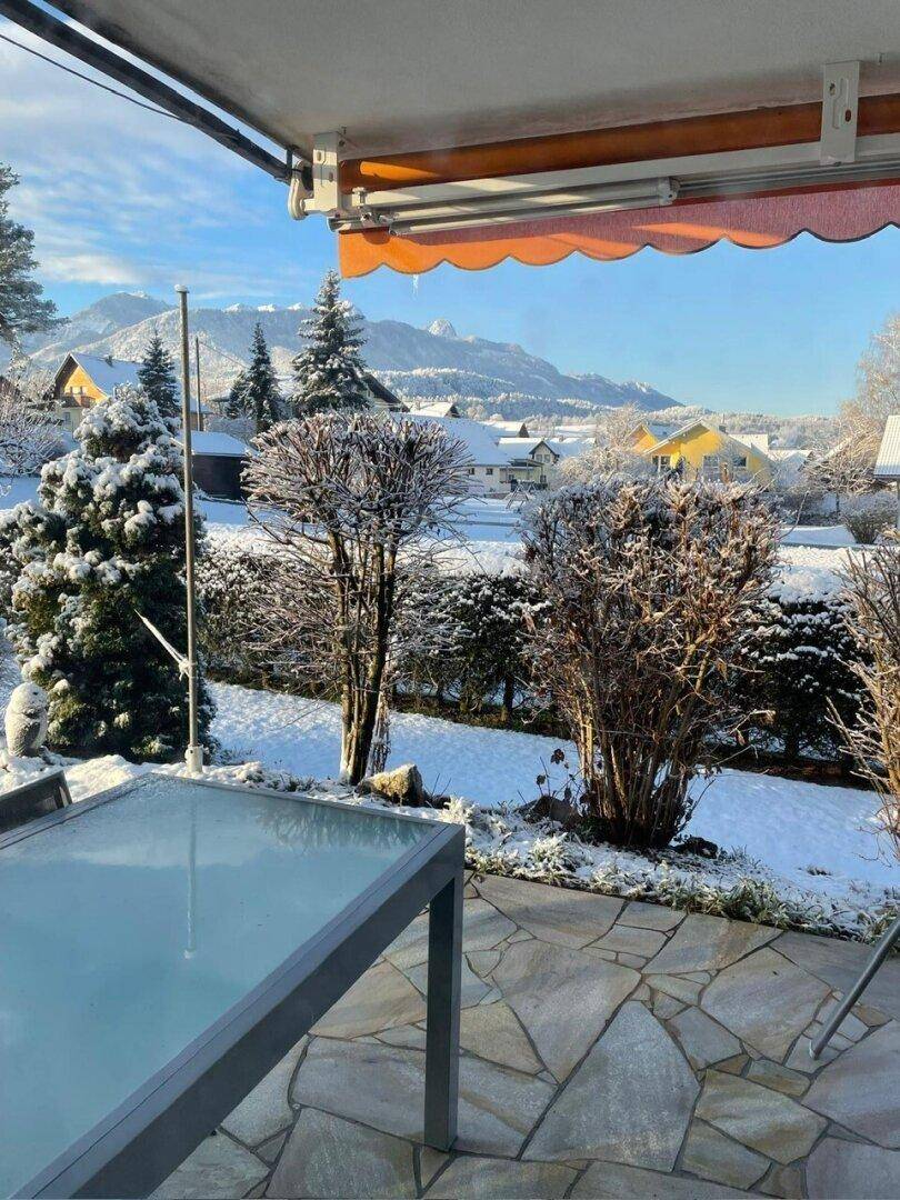 Gemütliche Terrasse mit Steinfliesen, Gartenmöbeln und verschneiter Berglandschaft im Hintergrund.