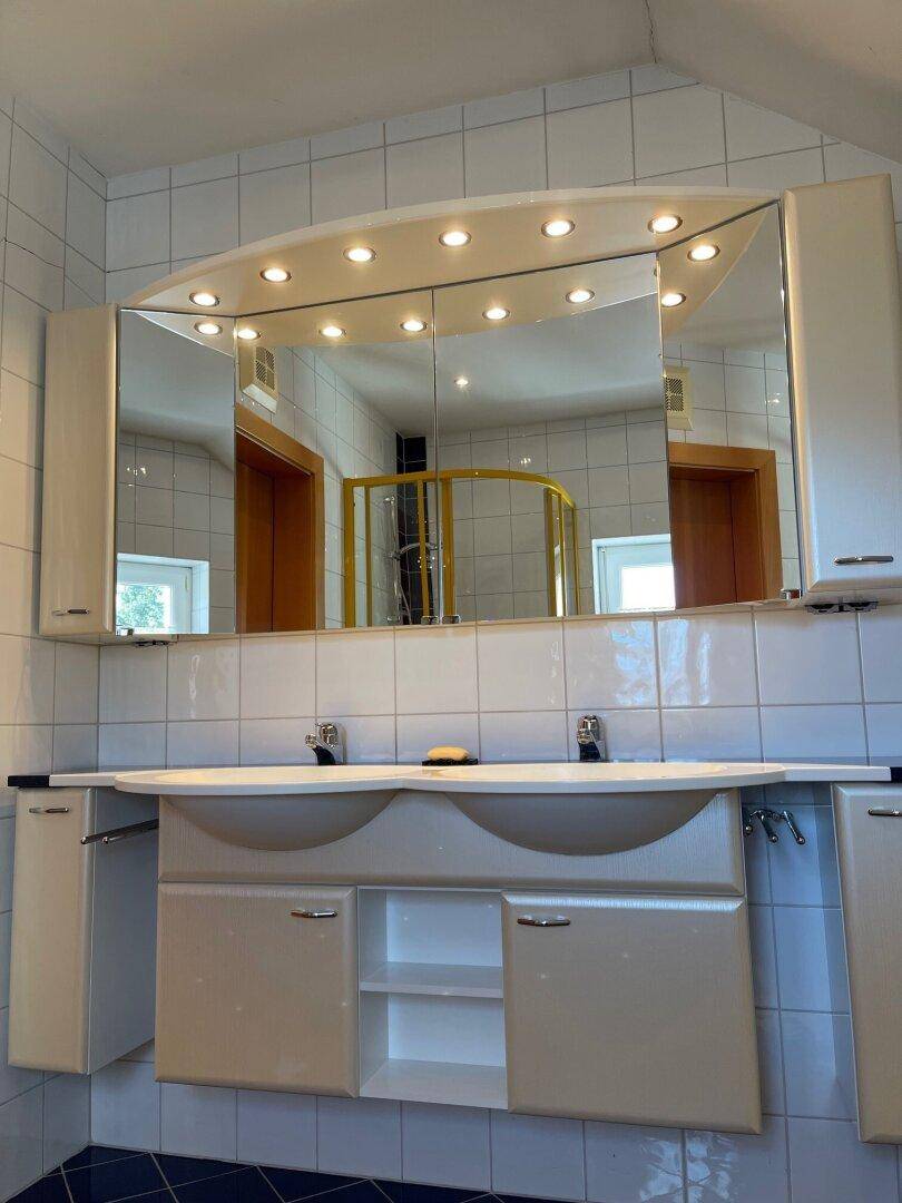Badezimmer mit Doppelwaschbecken, Spiegelschrank und integrierter Beleuchtung.