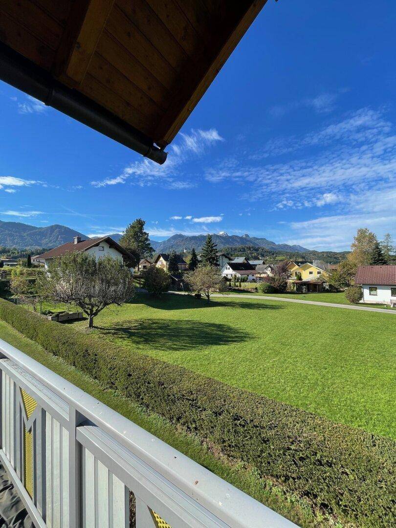 Balkon mit weitem Blick über grüne Landschaft und Berge unter blauem Himmel.