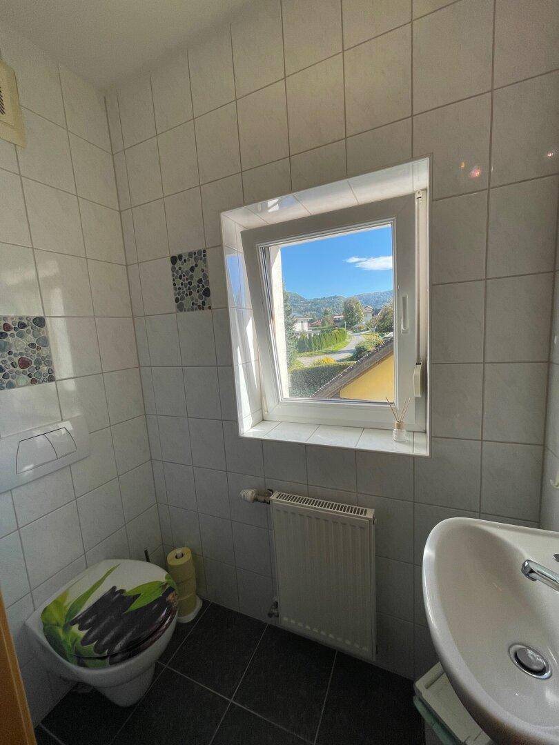Kleines Gäste-WC mit Fenster, weißen Fliesen und Blick ins Grüne.
