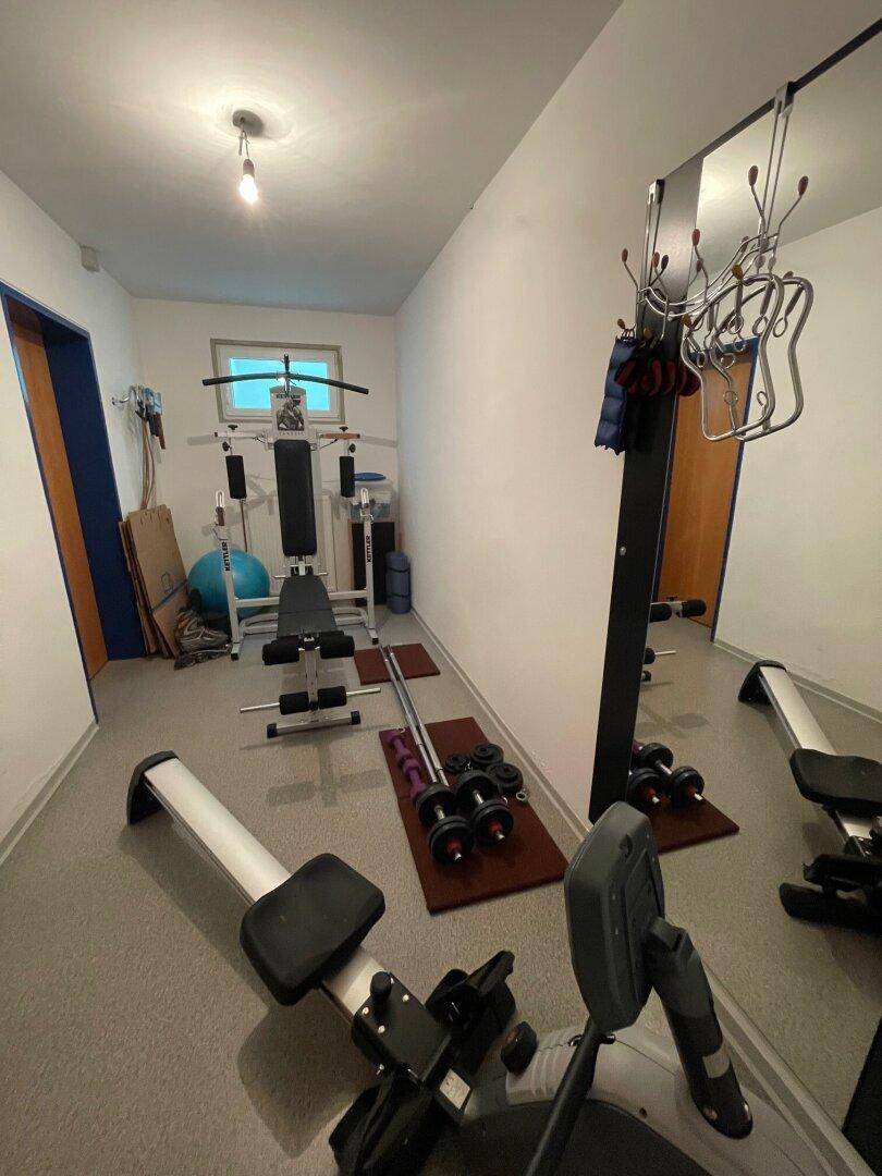 Geräumiger Fitnessraum im Keller mit verschiedenen Trainingsgeräten und einem Spiegel.