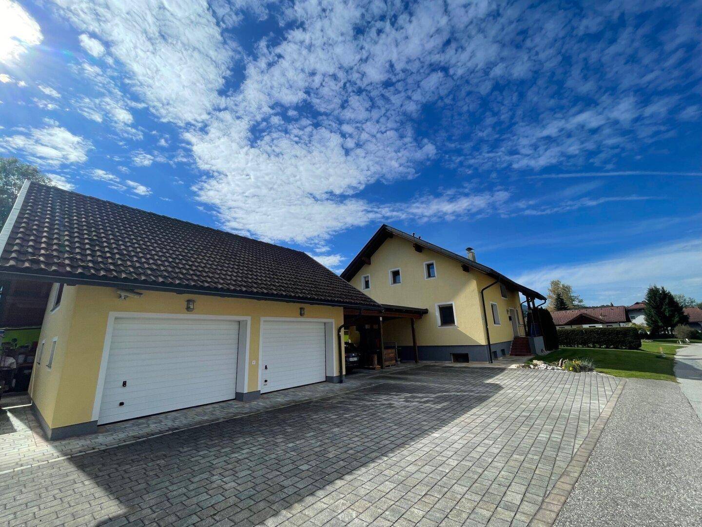 Gelbes Einfamilienhaus mit Doppelgarage und gepflasterter Zufahrt unter blauem Himmel.