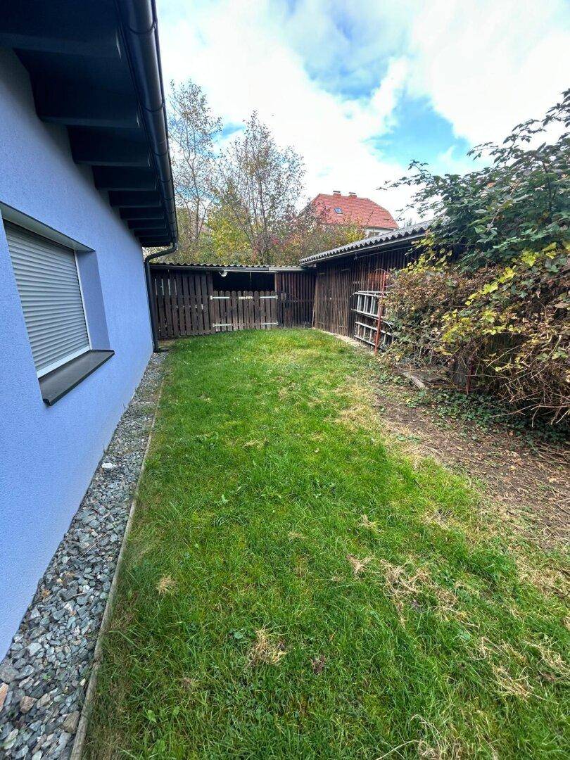 Langer, schmaler Gartenbereich mit Rasen und einem Holzschuppen im Hintergrund.