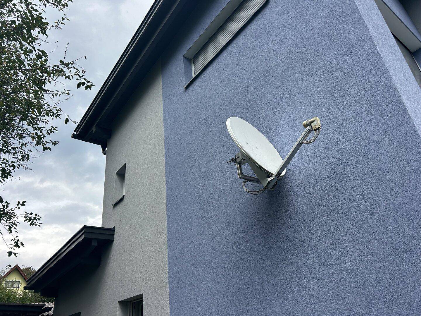 Detailansicht der blauen Hausfassade mit Satellitenschüssel und einem kleinen Fenster.