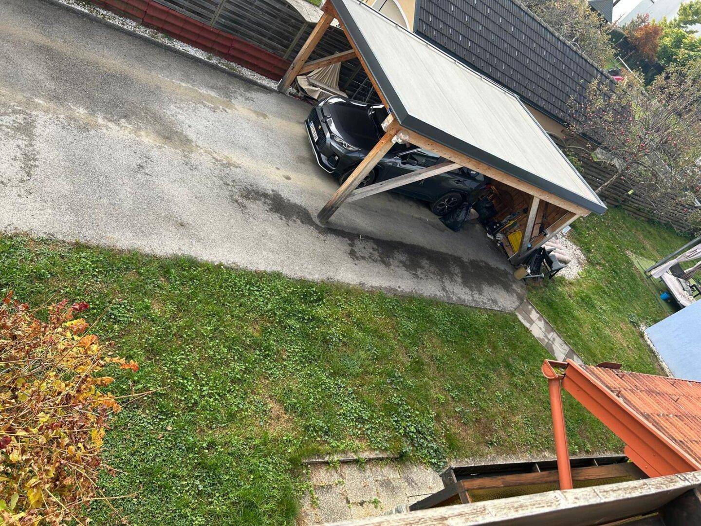 Vogelperspektive auf den Carport mit geparktem Auto und die Zufahrt des Grundstücks.