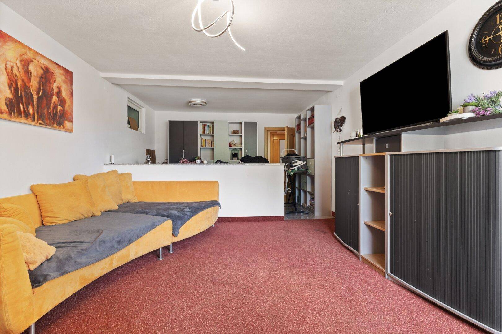 Wohnzimmer mit gelbem Sofa, Teppichboden und Blick auf den offenen Bereich.