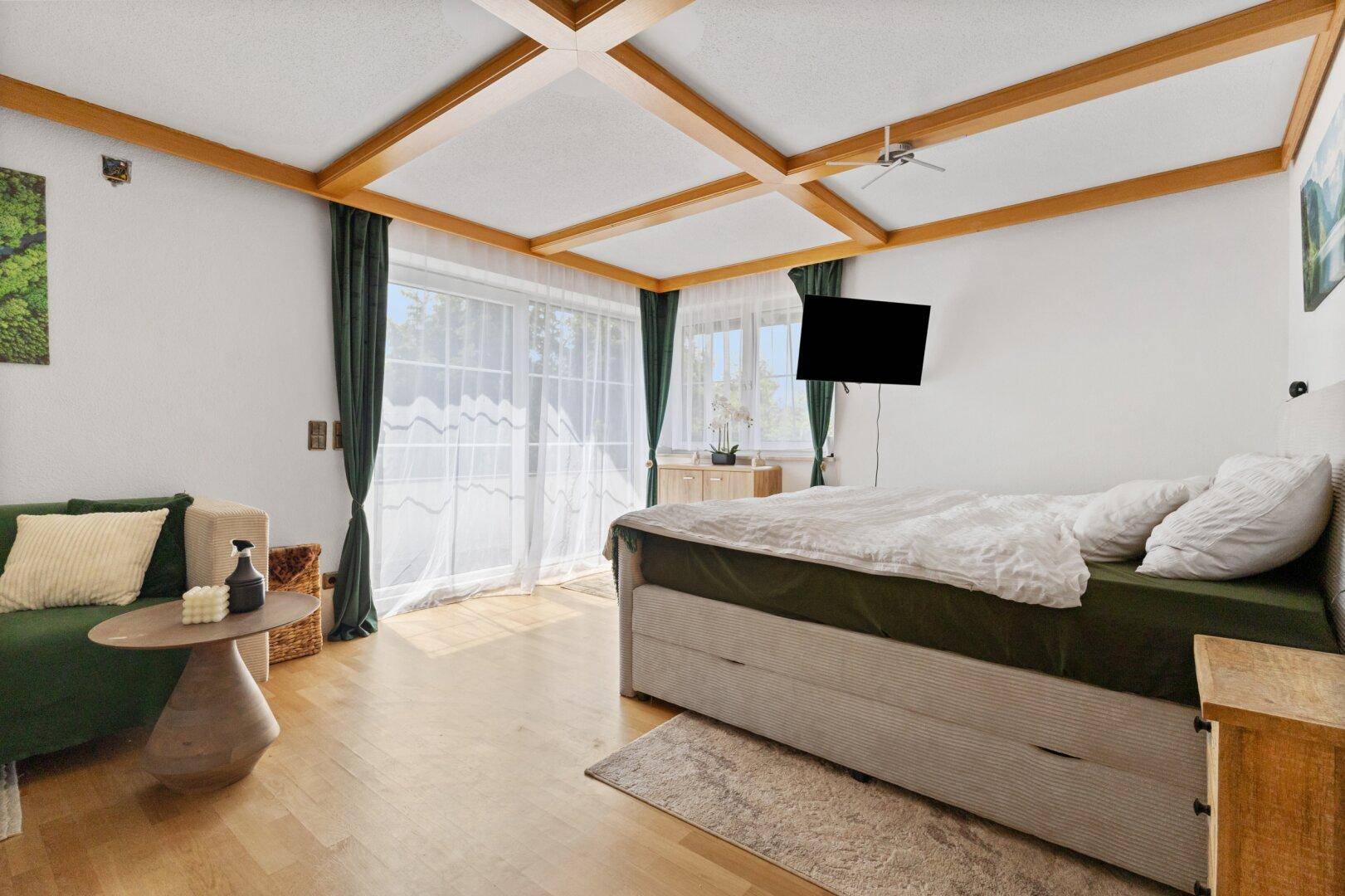 Helles Schlafzimmer mit Holzbalkendecke, Parkettboden und Zugang zum Balkon.