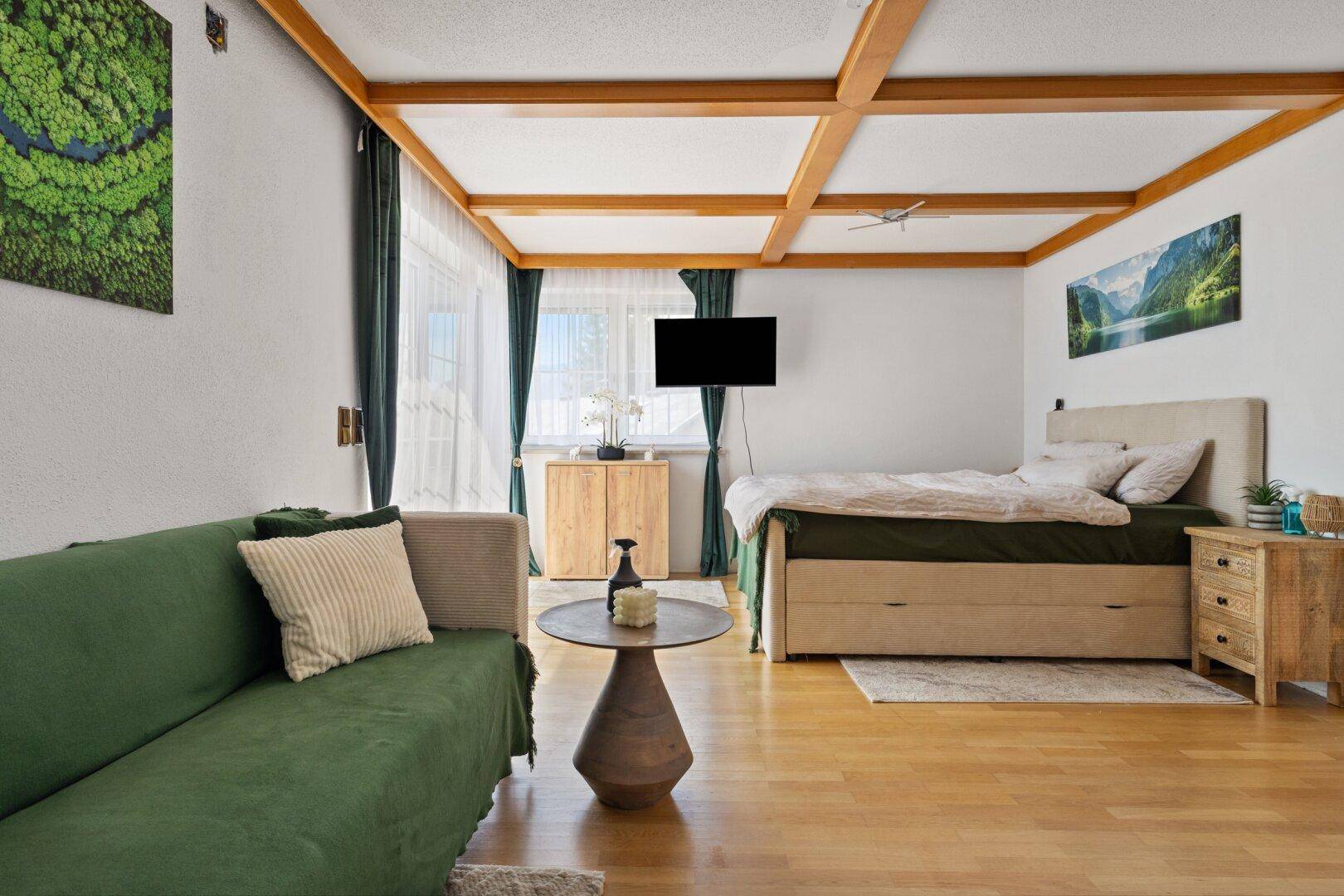 Schlafzimmer mit Holzbalkendecke, Parkettboden und gemütlichem Sofa.