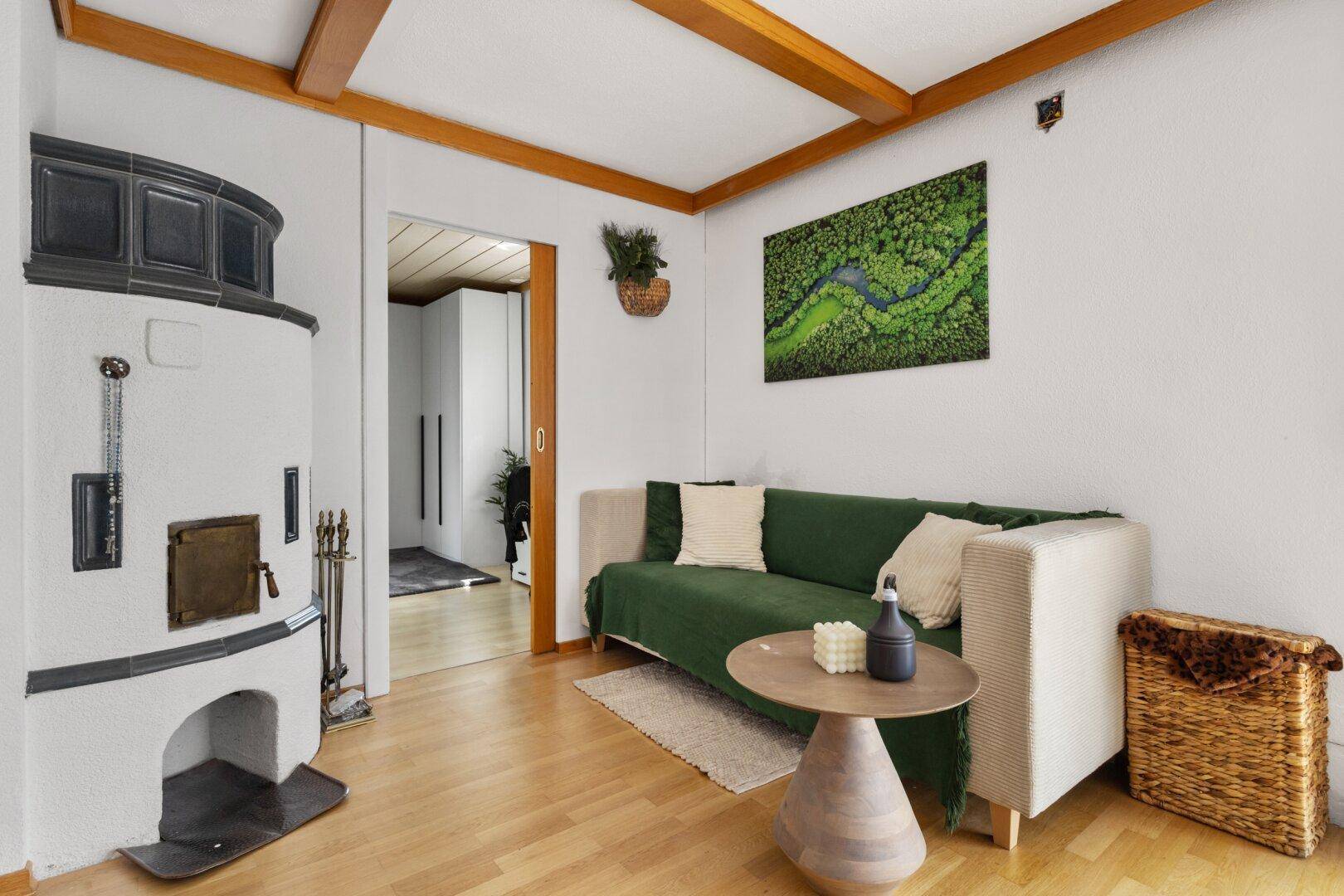Gemütlicher Bereich im Schlafzimmer mit Sofa, Kachelofen und Holzbalkendecke.