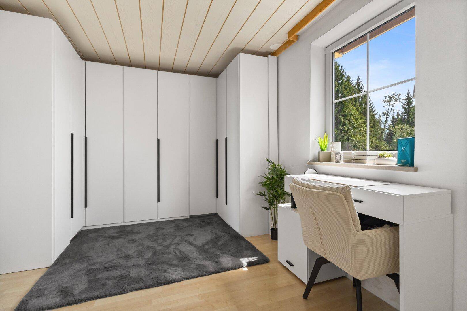 Helles Arbeitszimmer mit Einbauschränken, Schreibtisch und Blick ins Grüne.