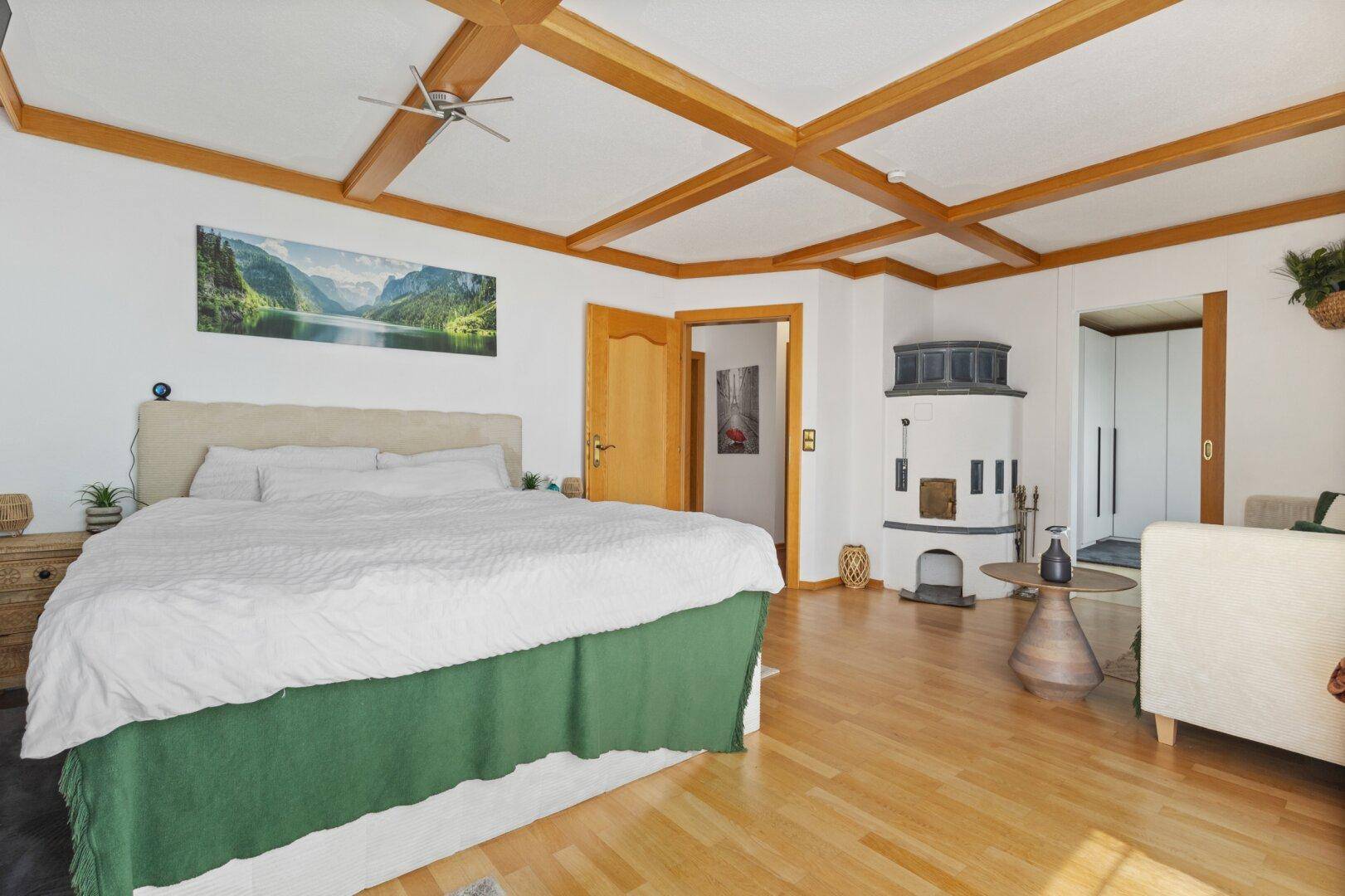 Geräumiges Schlafzimmer mit Holzbalkendecke, Parkettboden und traditionellem Kachelofen.