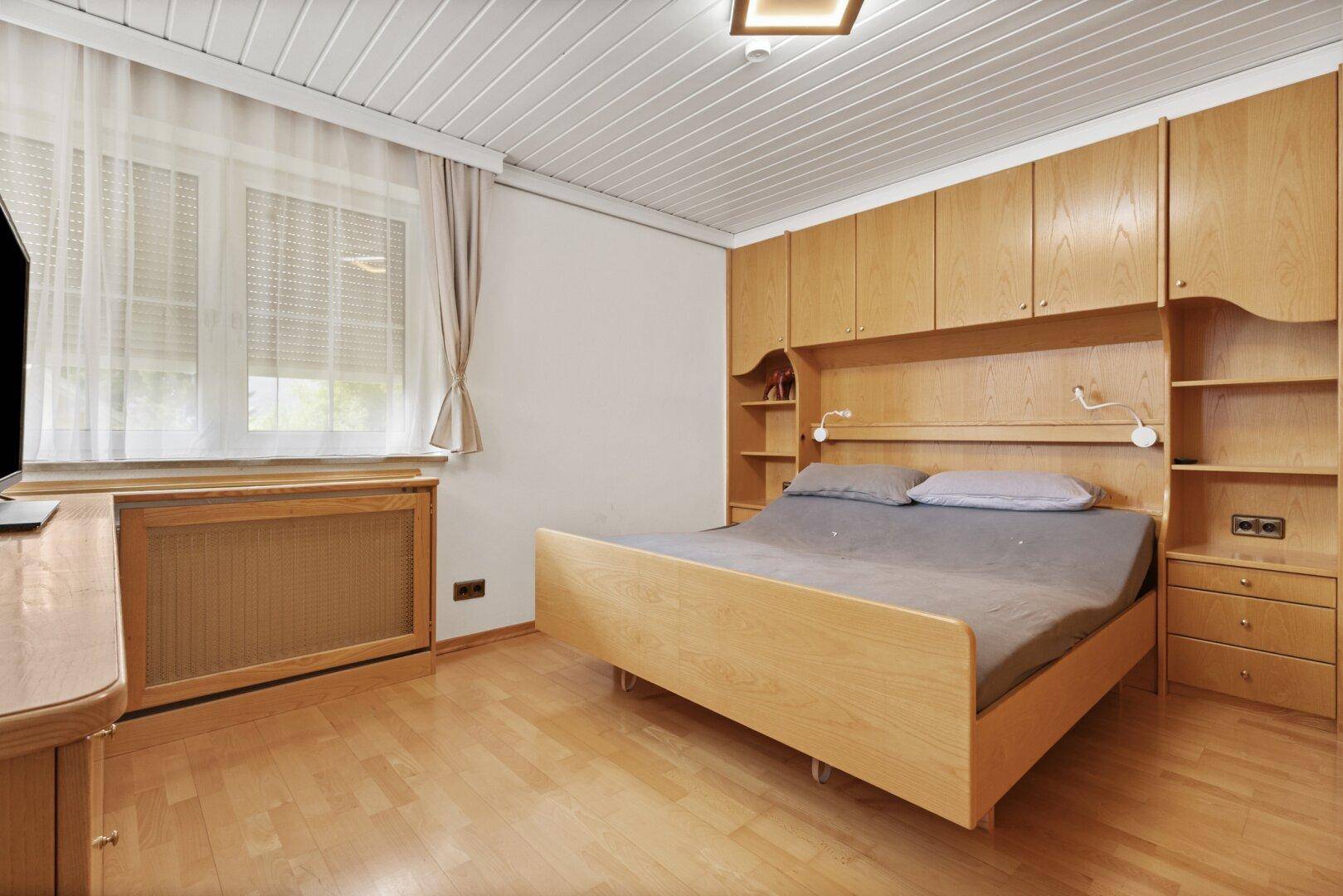Schlafzimmer mit Holzvertäfelung an der Decke, Einbauschränken und Parkettboden.