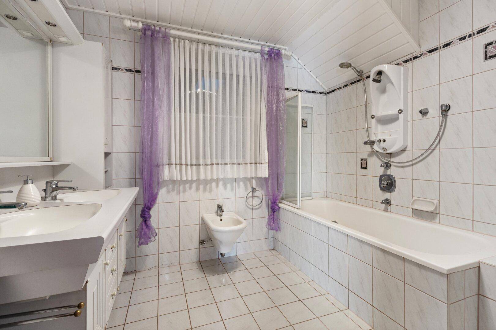Badezimmer mit Badewanne, Bidet, Dusche und Fliesenboden in Weiß.