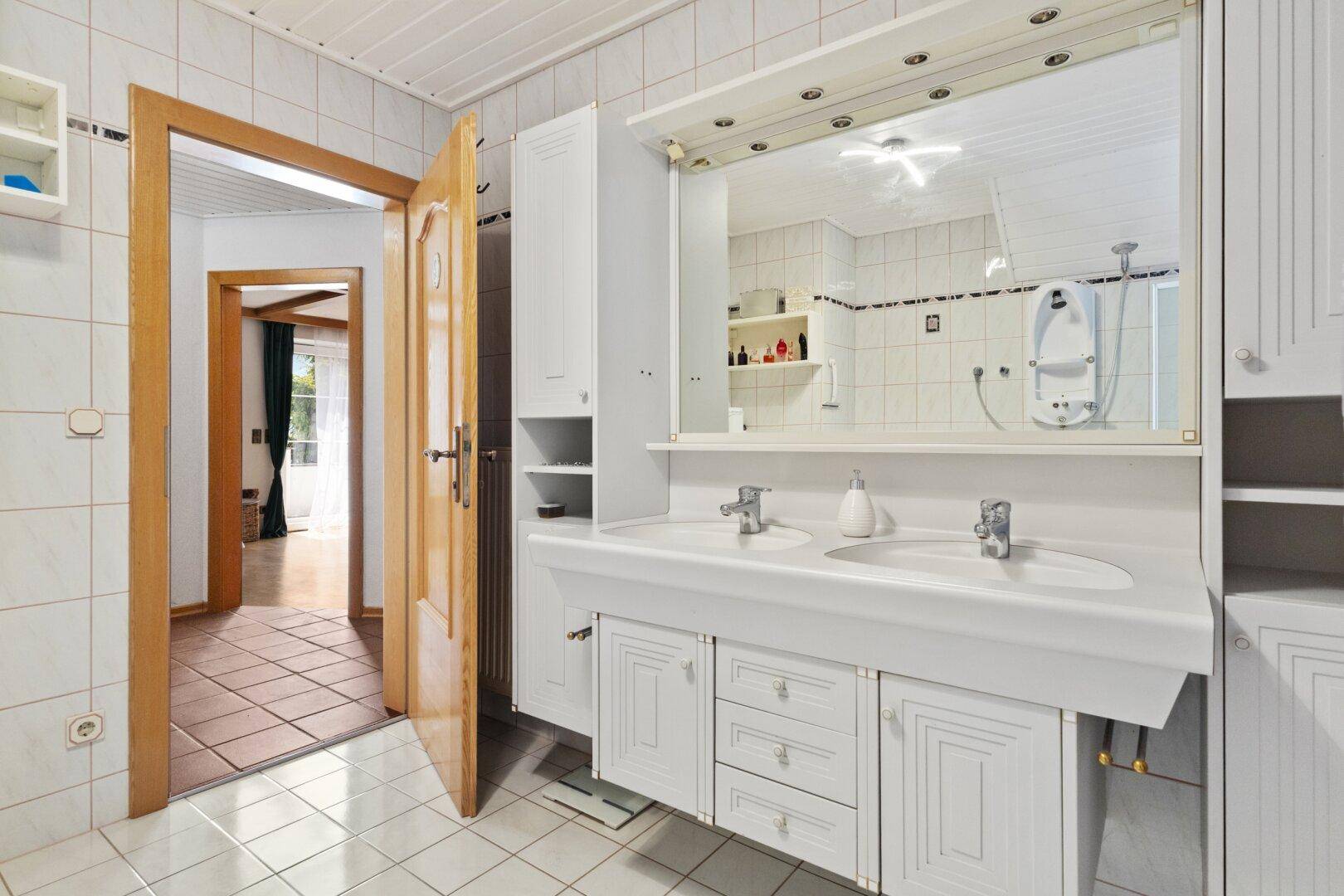 Badezimmer mit Doppelwaschbecken, großem Spiegel und weißen Fliesen.
