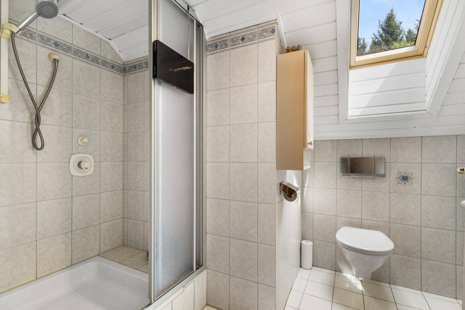 Helles Badezimmer mit Dusche, WC, Fliesen und einem Dachfenster für Tageslicht.