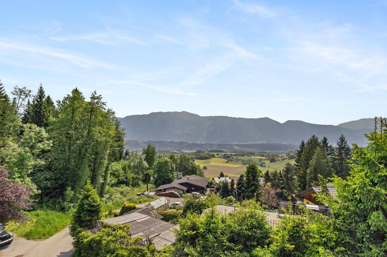 Panoramablick auf die grüne Landschaft mit Bergen und vereinzelten Häusern in der Ferne.