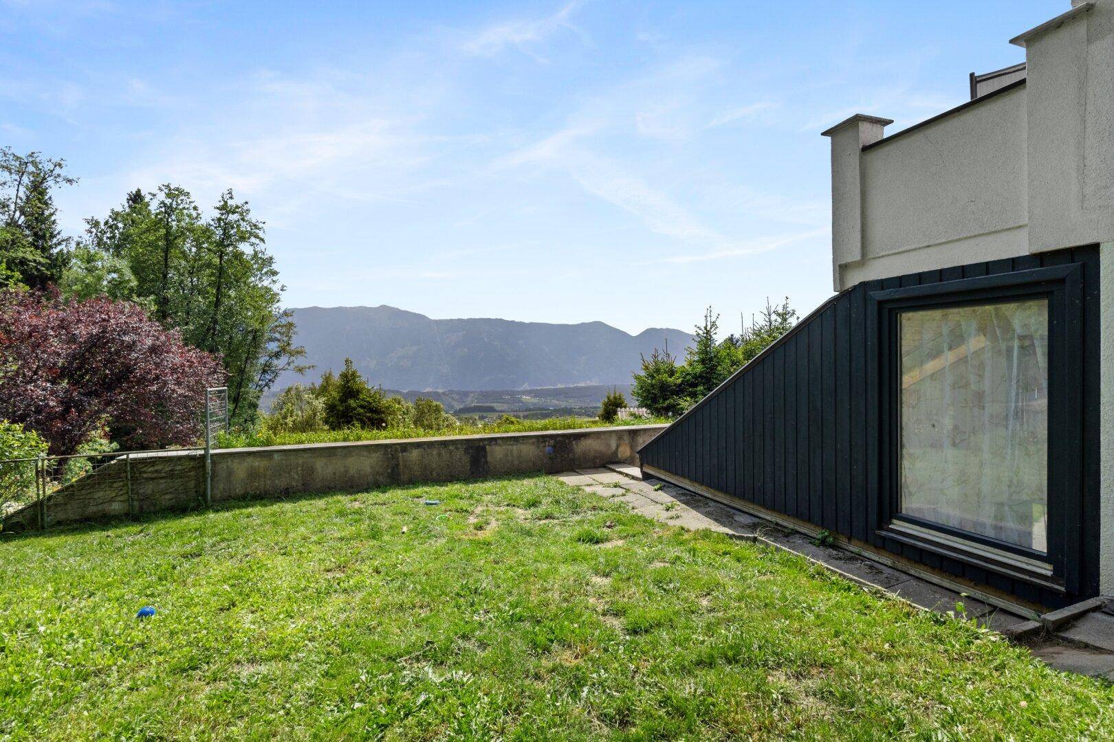 Rasenfläche im Gartenbereich mit Betonmauer und weitem Blick auf die Berglandschaft.