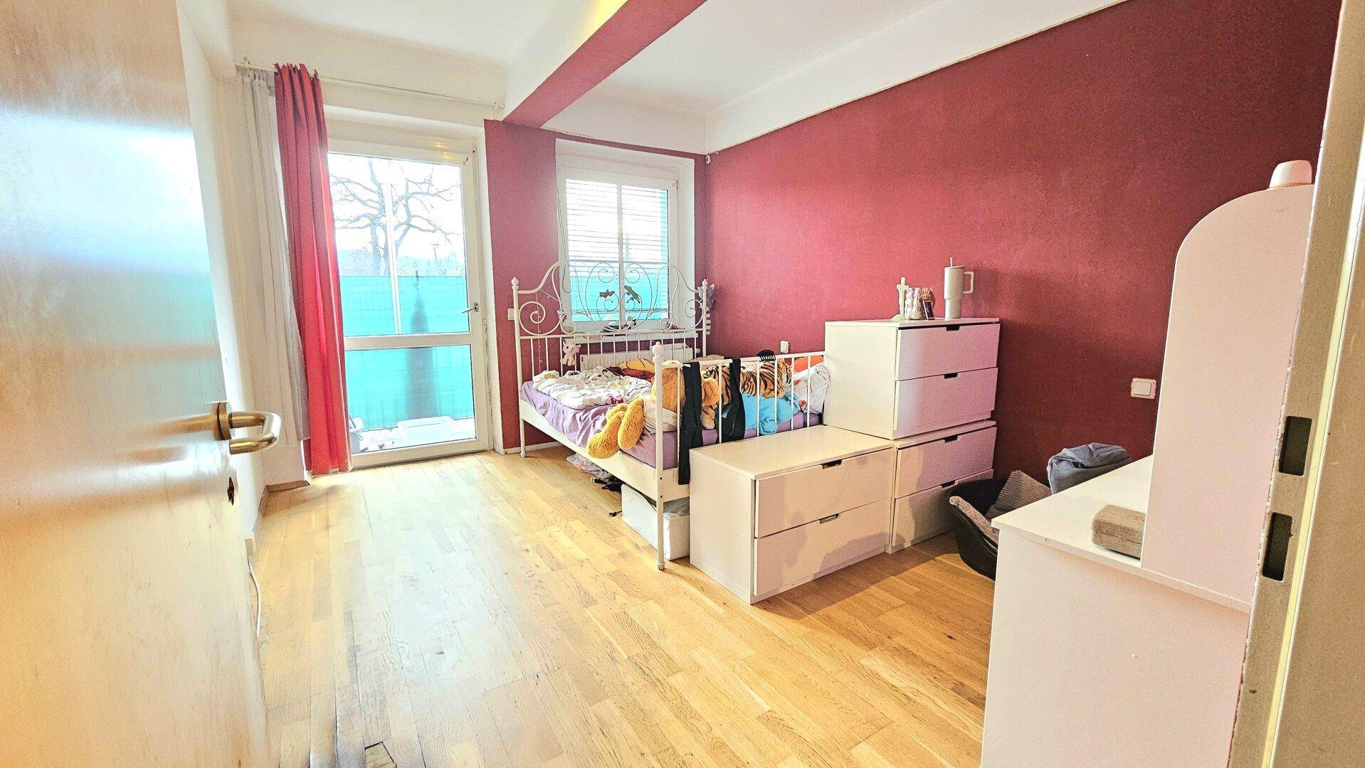 Kinderzimmer mit roter Wand, Einzelbett und direktem Zugang zum Balkon.