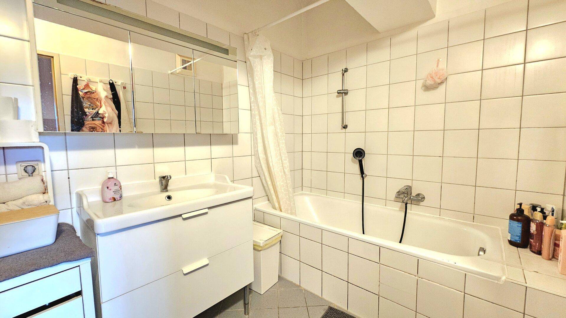 Badezimmer mit Badewanne, Waschbecken, Spiegelschrank und weißen Fliesen.