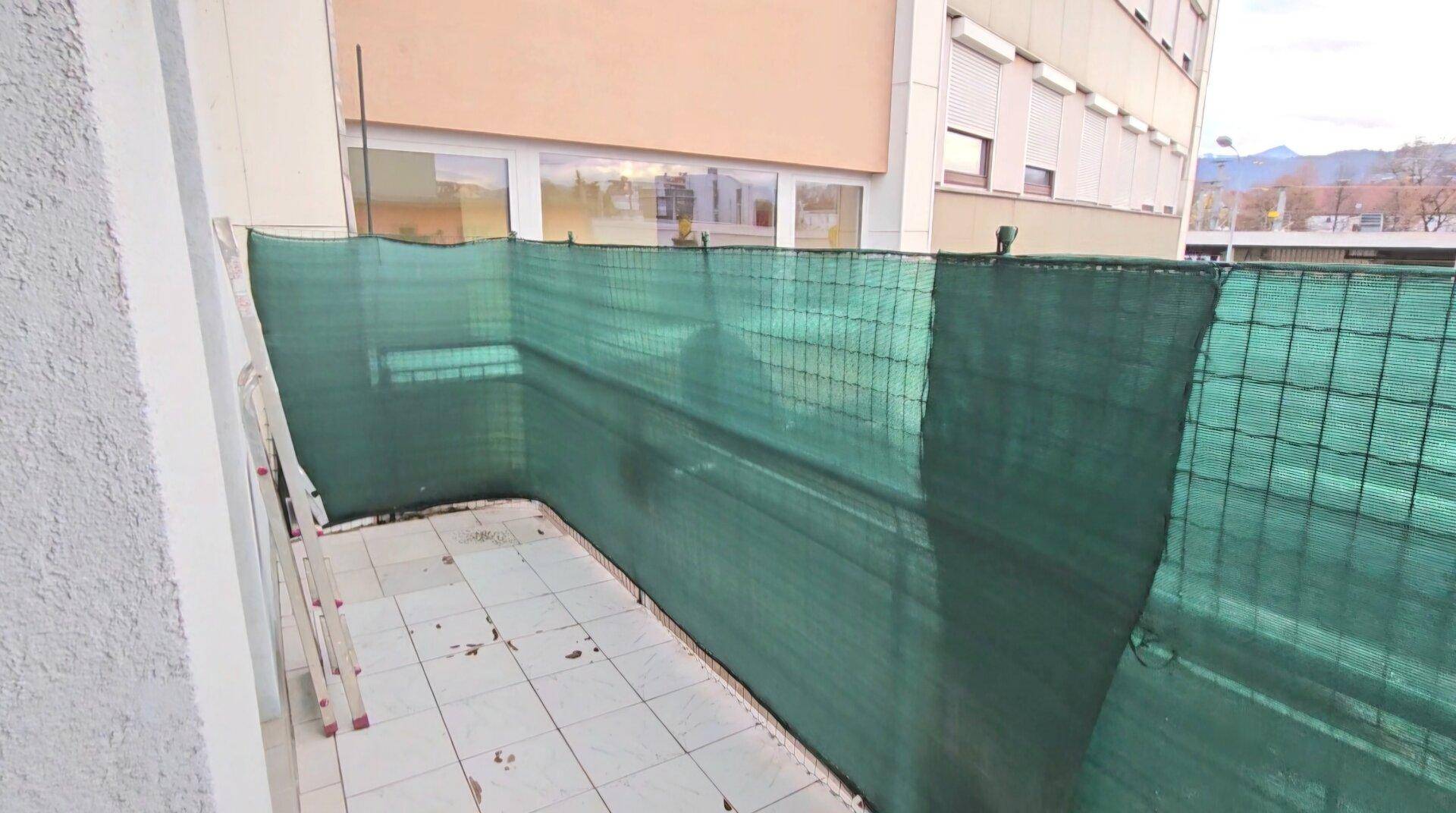 Balkon mit Fliesenboden und grüner Sichtschutzverkleidung für Privatsphäre.