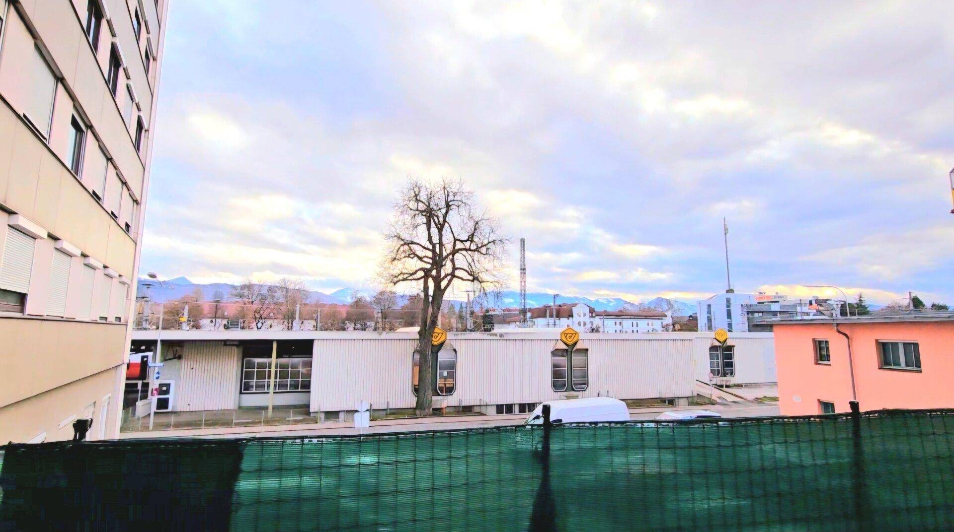 Blick vom Balkon auf die städtische Umgebung mit Gebäuden und Bergen im Hintergrund.