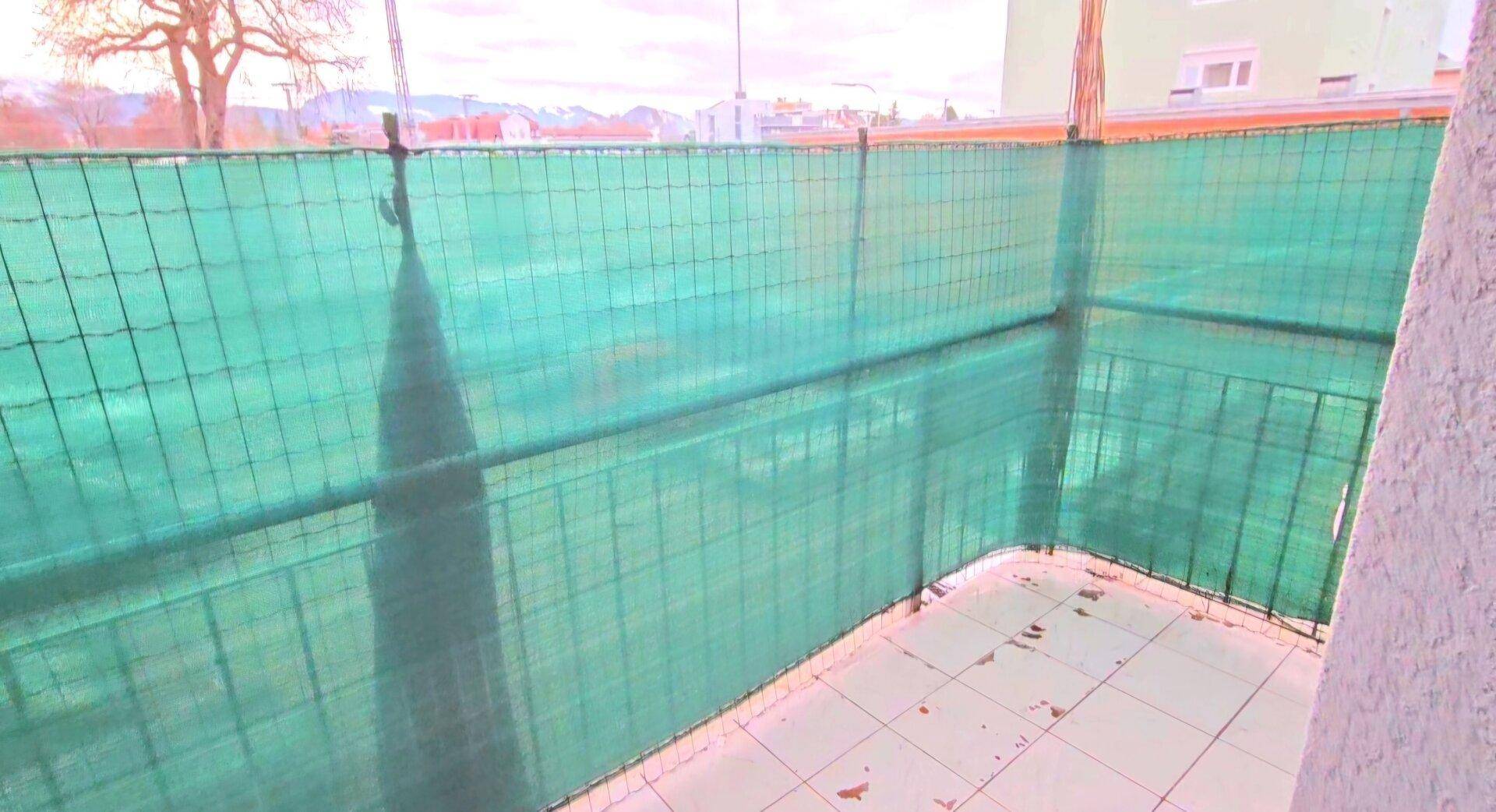 Balkon mit Fliesenboden und grüner Sichtschutzverkleidung, bietet einen geschützten Außenbereich.