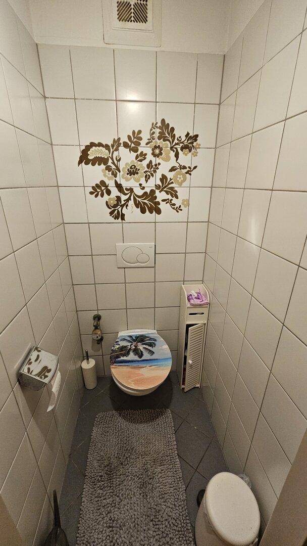 Kleines WC mit weißen Fliesen, Wand-WC und dekorativer Wandgestaltung.