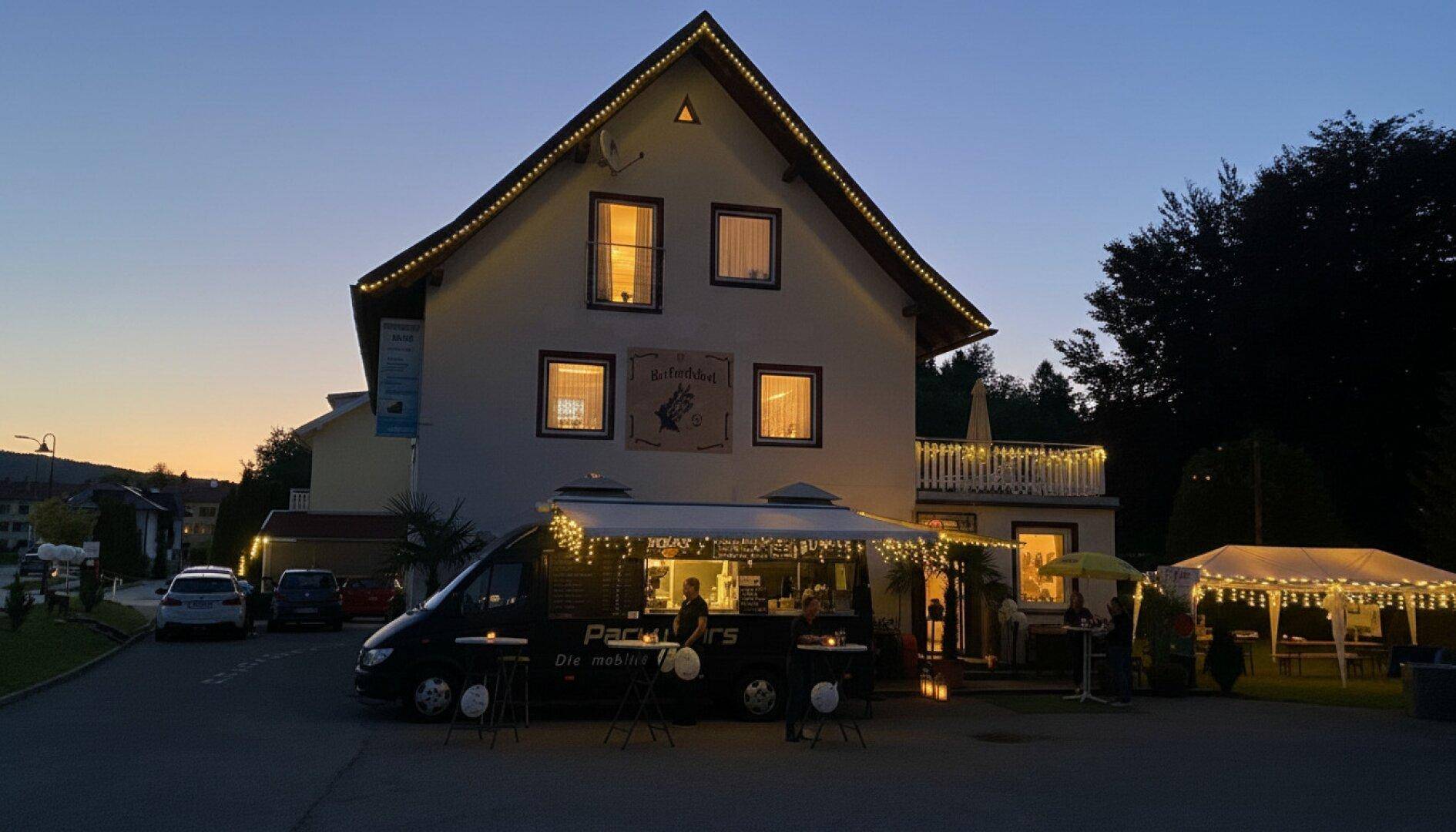 Gebäude bei Dämmerung, festlich beleuchtet mit Lichterketten, einem Foodtruck und Partyzelt.