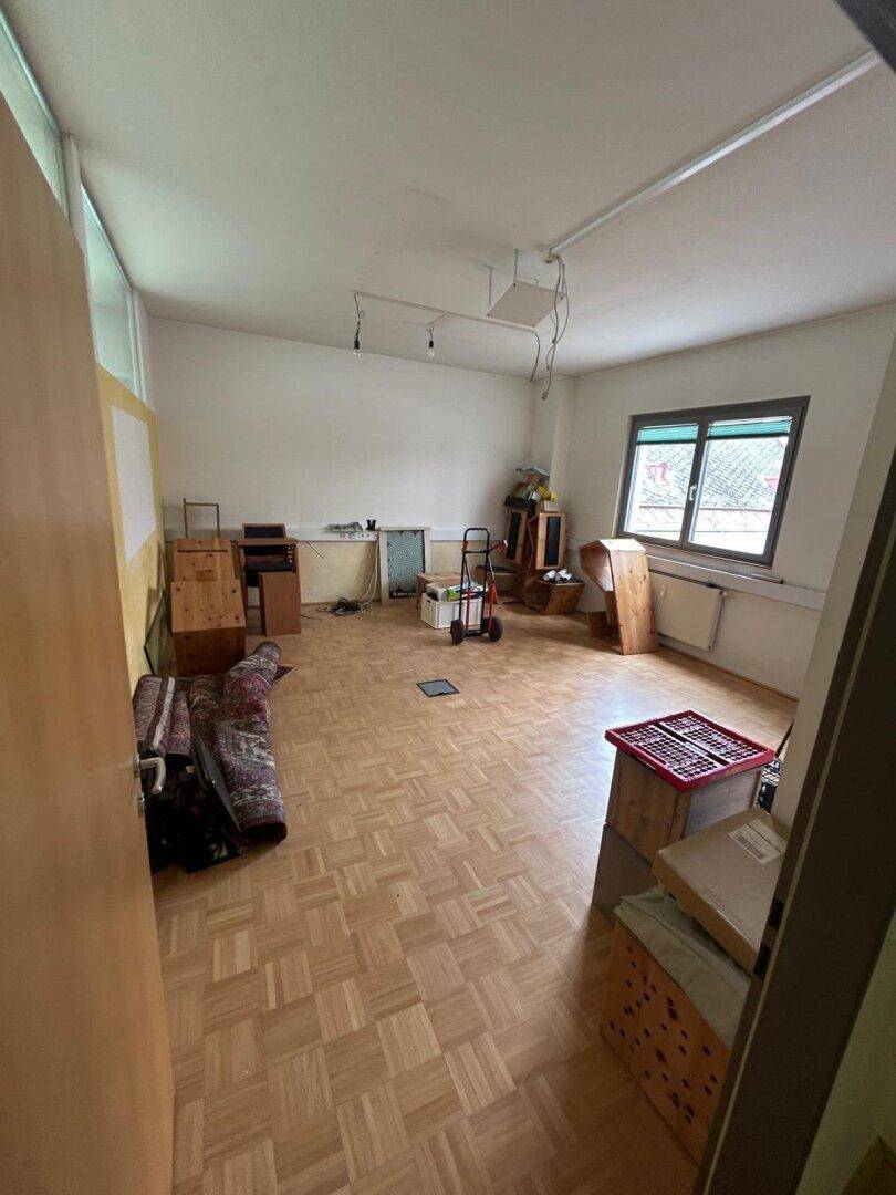 Geräumiger Raum mit Parkettboden und einem Fenster, derzeit als Lagerfläche genutzt.