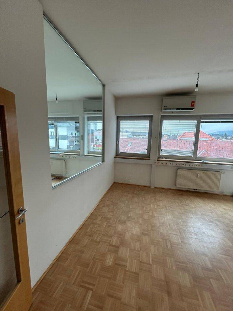 Heller Raum mit Parkettboden, großen Fenstern und einem Wandspiegel, ideal für Büro oder Wohnen.