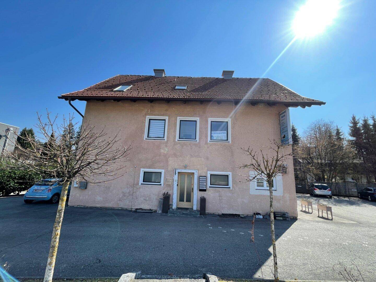 Rückansicht des Gebäudes mit Satteldach und Parkplätzen unter strahlendem Sonnenschein.