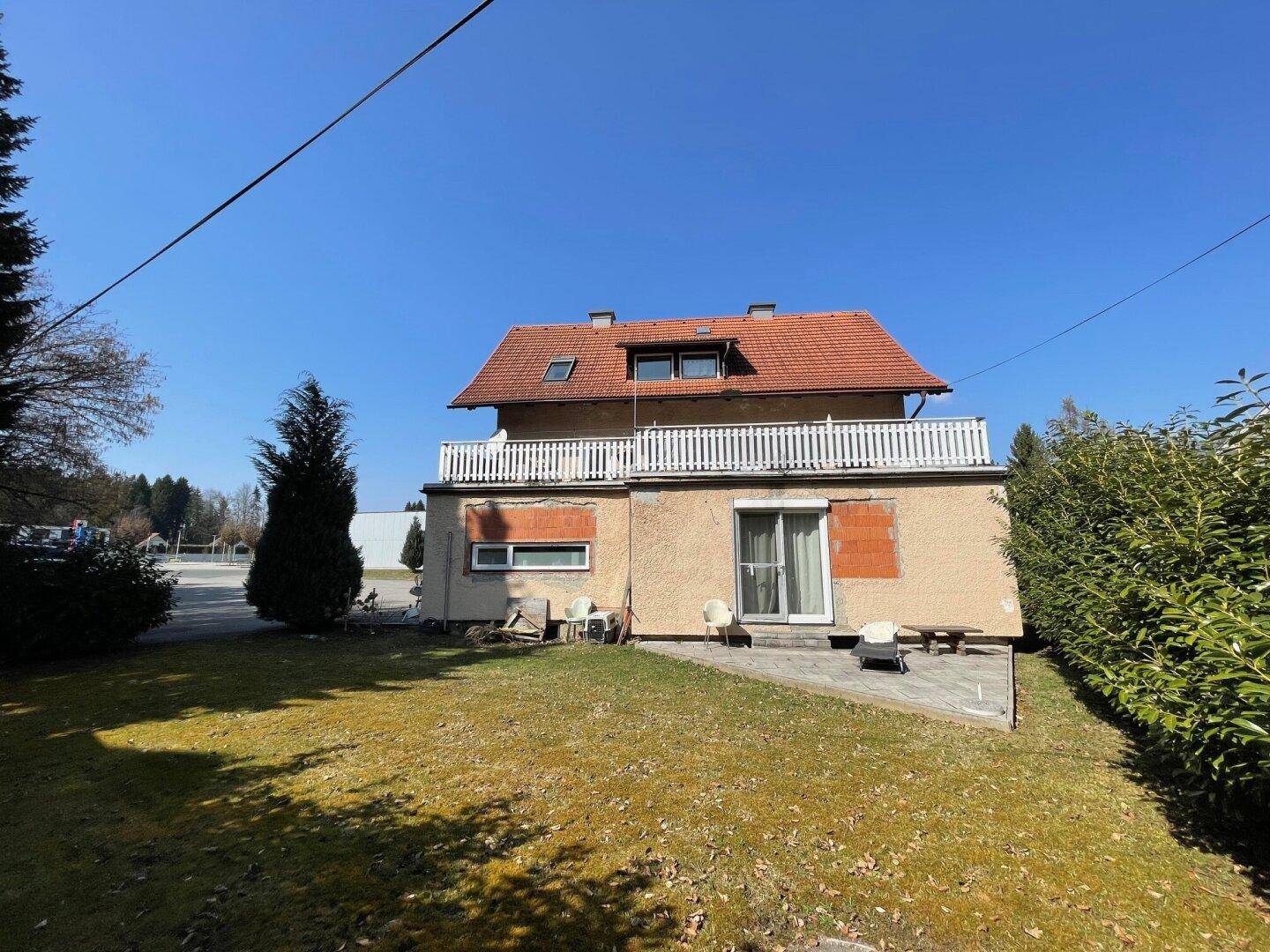 Rückansicht des Gebäudes mit gepflegtem Rasen, Terrasse und Balkon im Obergeschoss.