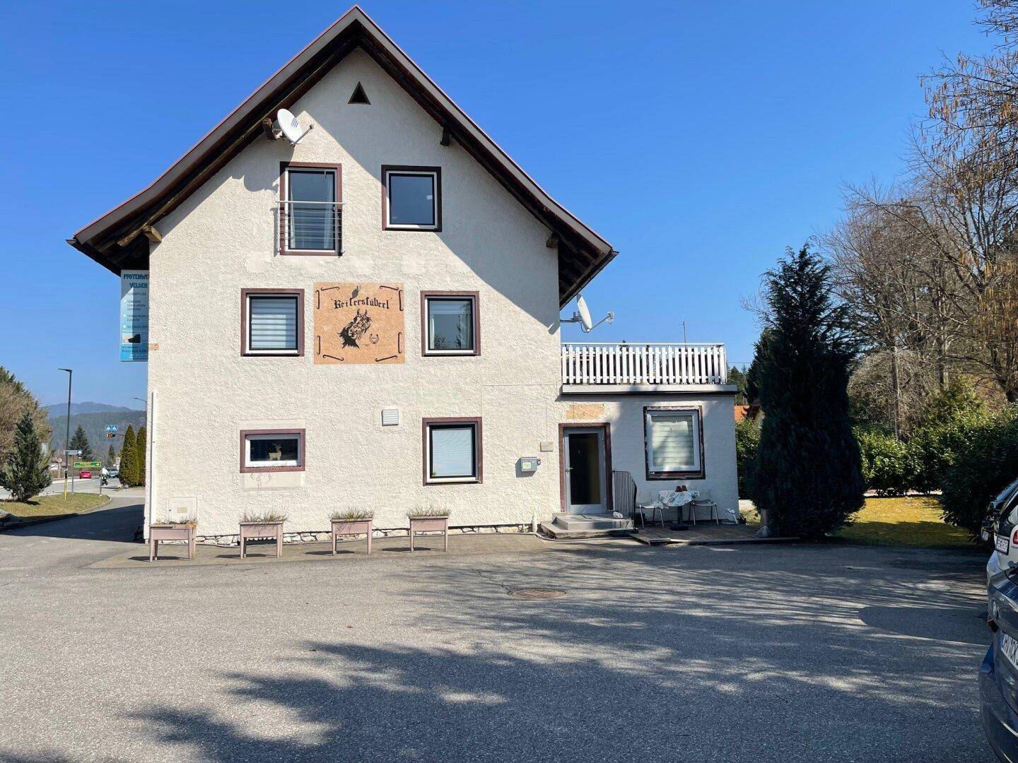 Gebäudeansicht von vorne mit Blumenkästen und einem kleinen Balkon im Obergeschoss.
