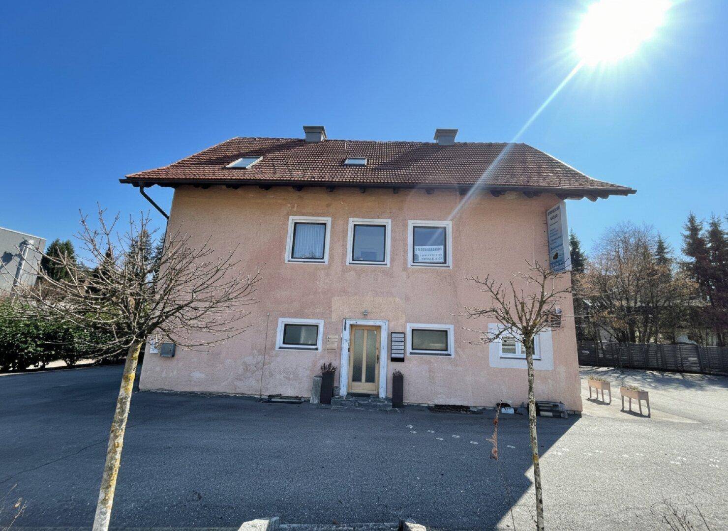 Vorderansicht des Gebäudes mit Satteldach und Fenstern unter strahlendem Sonnenschein.