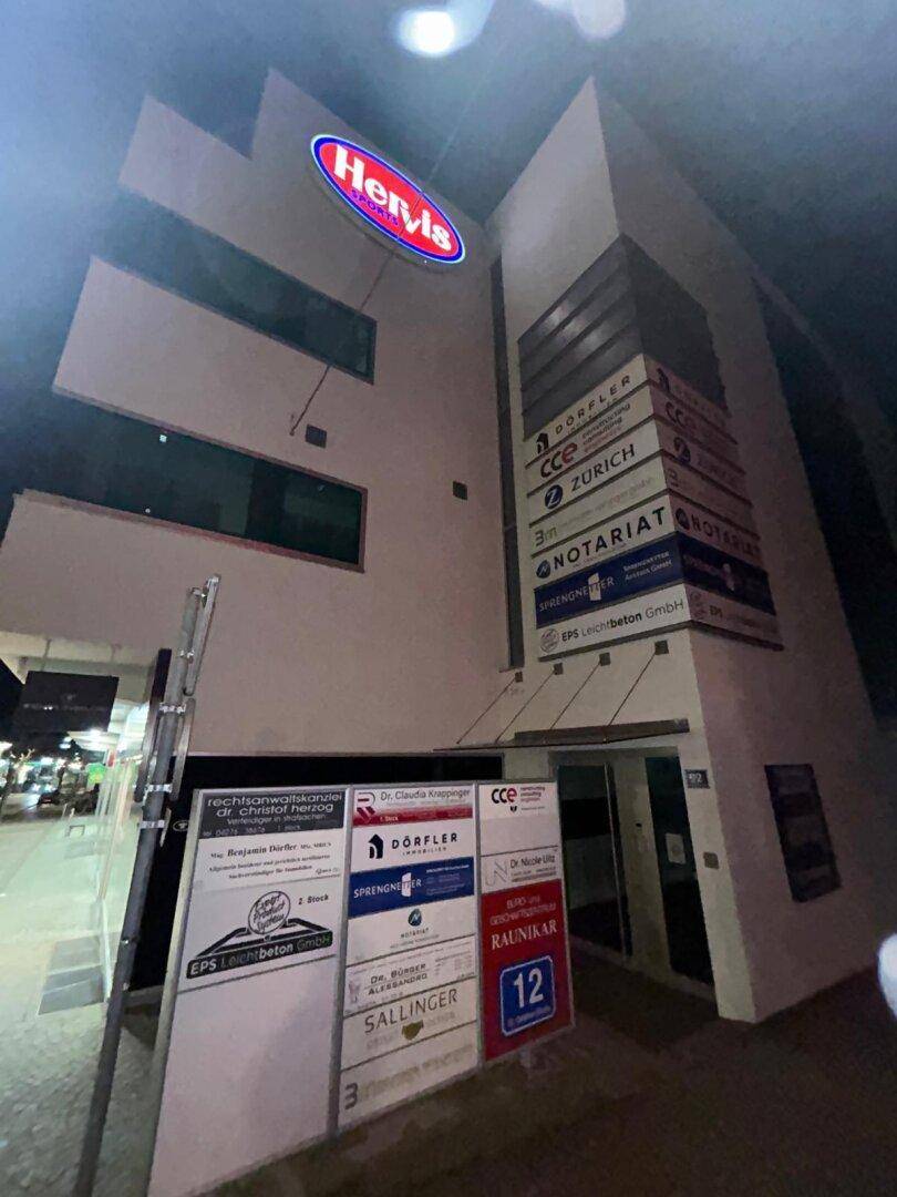 Geschäftsgebäude bei Nacht mit beleuchteten Werbeschildern und Ladenfronten an der Straße.