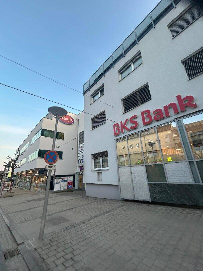 Ansicht eines modernen Geschäftsgebäudes mit angrenzender Bankfiliale an einer belebten Straße.