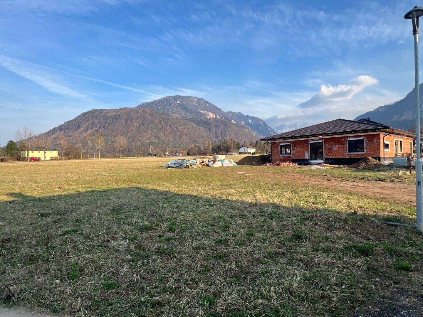 Unbebautes Grundstück mit einem im Bau befindlichen Haus und weitem Blick auf die umliegenden Berge.