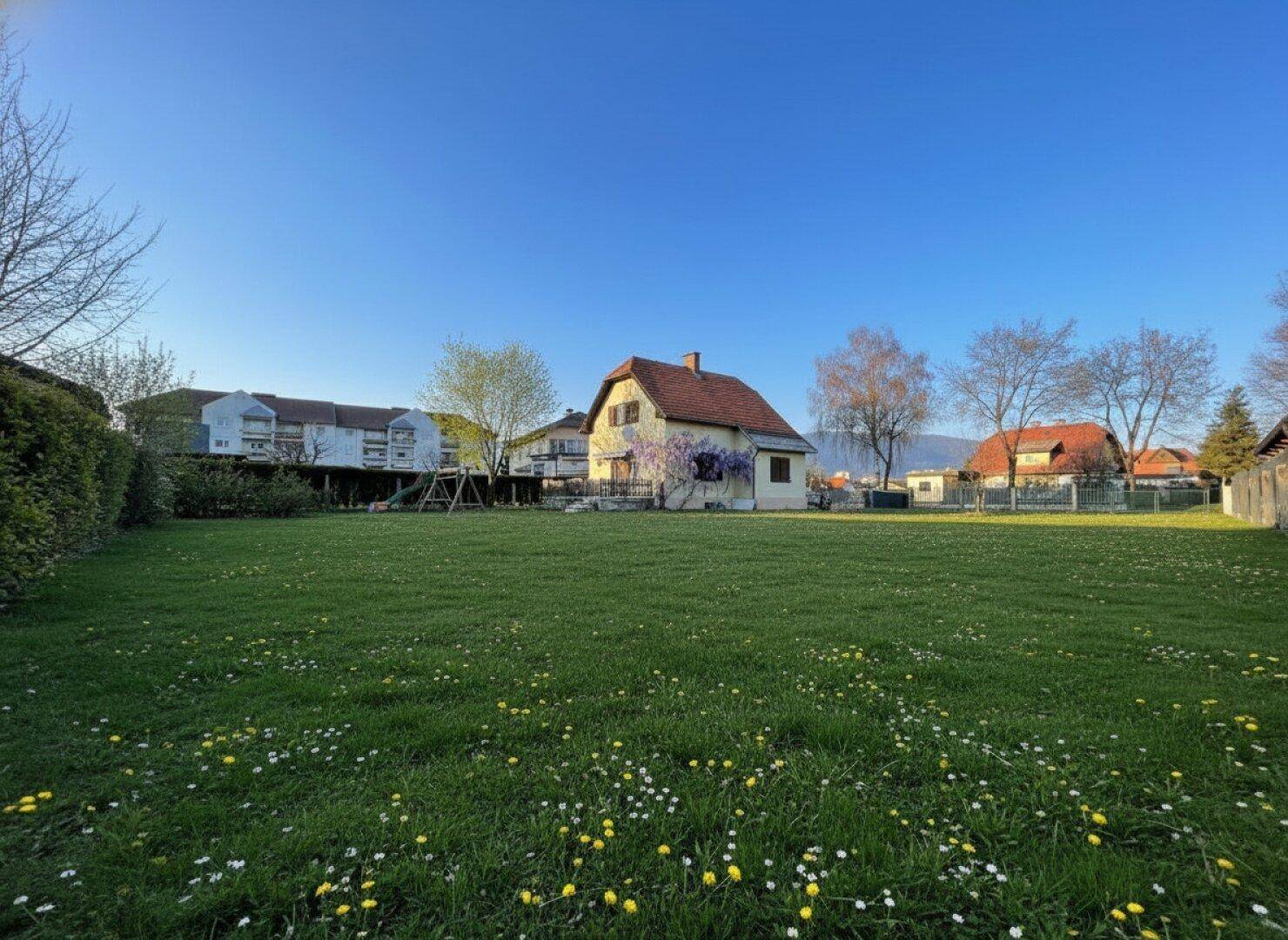 Weitläufiger Garten mit Haus im Hintergrund und Panoramablick auf die umliegende Berglandschaft.