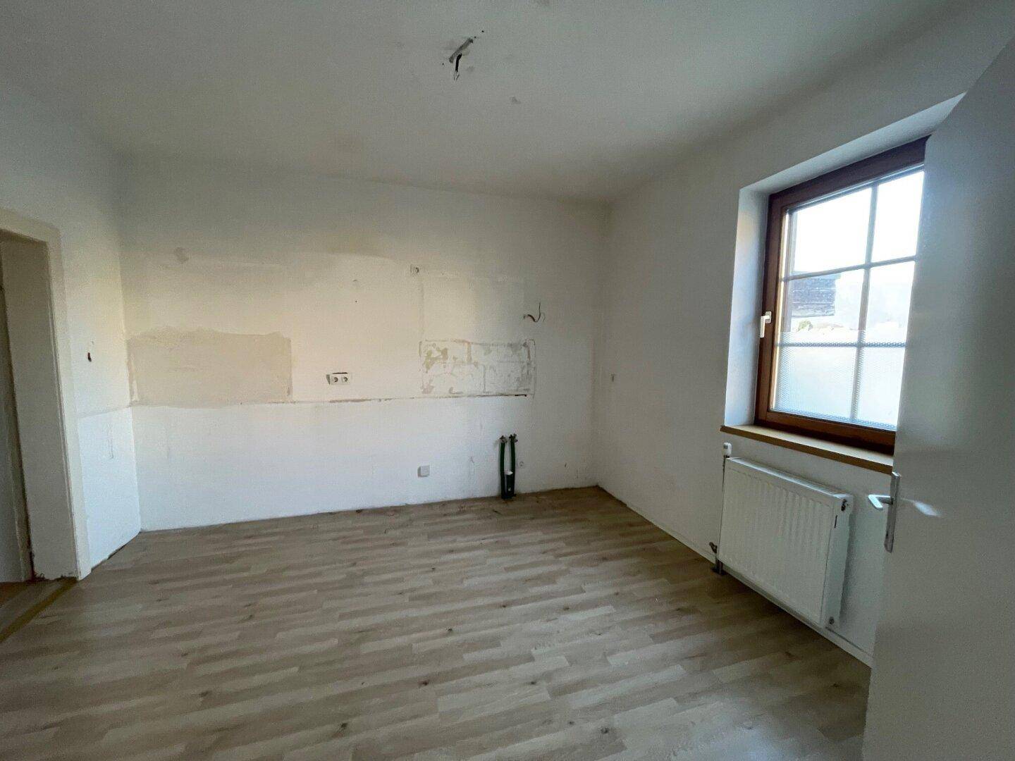 Leerer Raum, vorbereitet für eine Küche, mit Laminatboden und Fenster.
