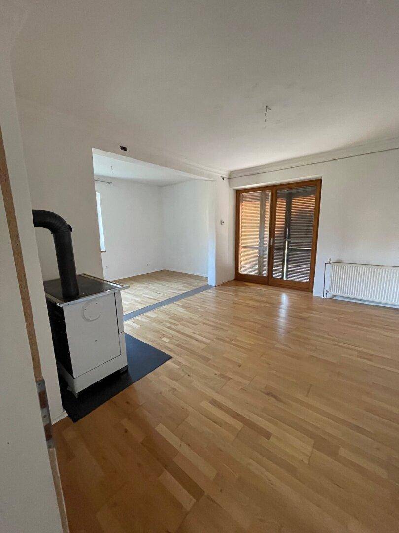 Geräumiges Wohnzimmer mit Parkettboden, Holzofen und Zugang zur Terrasse durch große Schiebetüren.