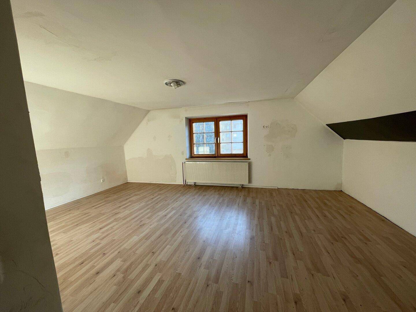 Helles Schlafzimmer im Dachgeschoss mit Laminatboden, Fenster und Dachschrägen.