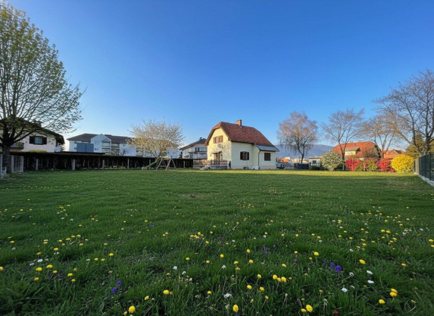 Weitläufiger Garten mit Haus im Hintergrund und Panoramablick auf die umliegende Berglandschaft.
