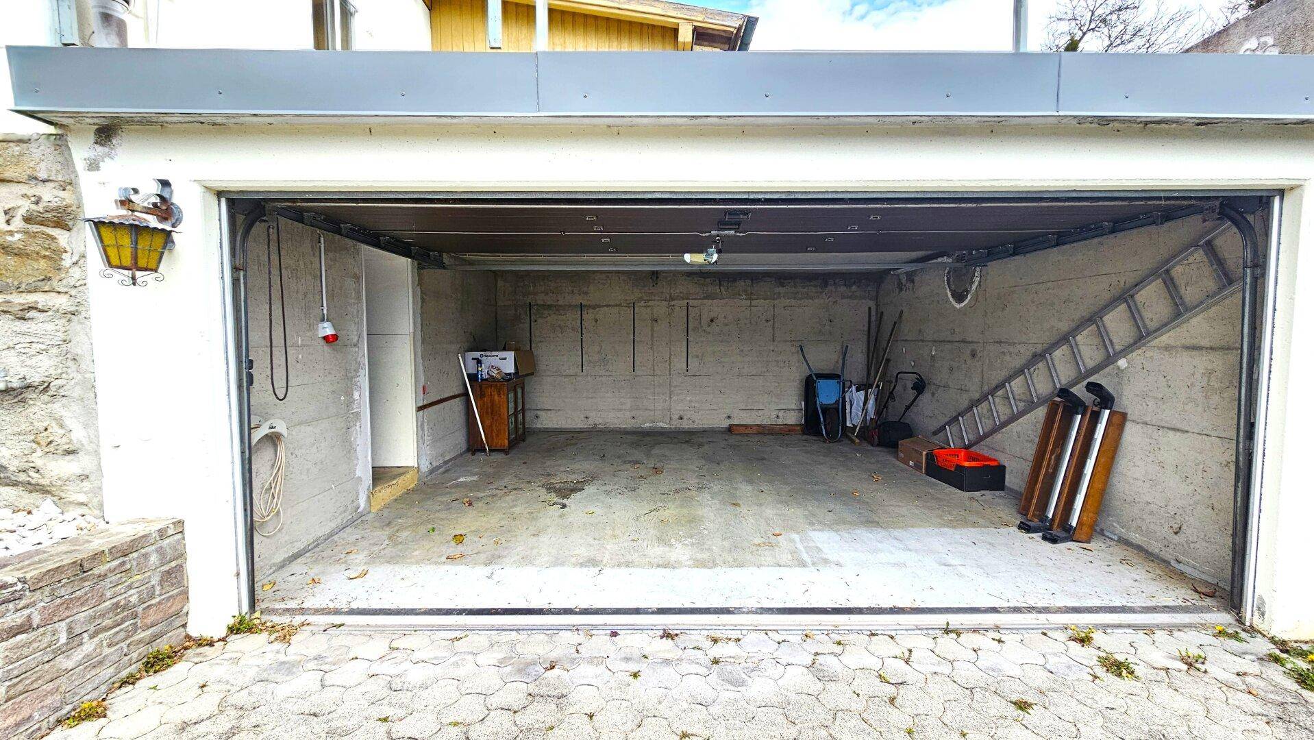 Geräumige Garage mit Betonboden, Leiter und verschiedenen Werkzeugen, bereit zur Nutzung.