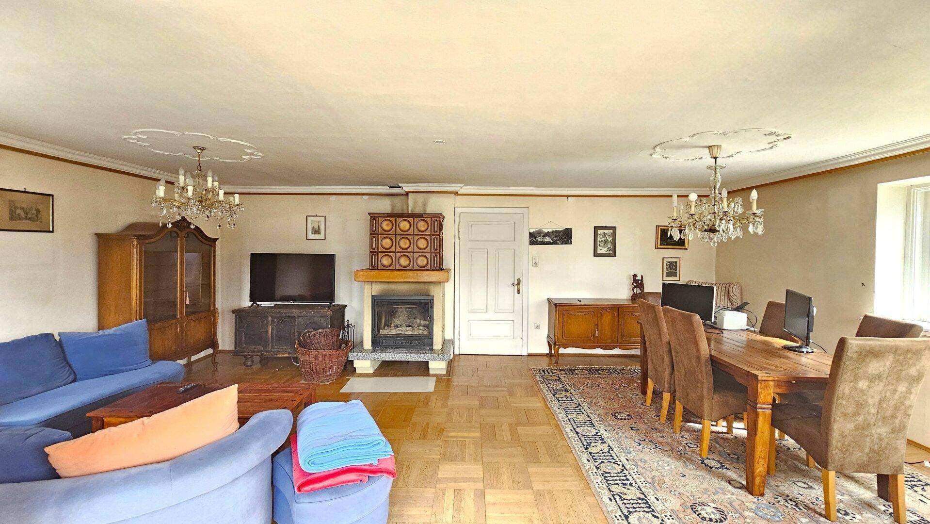 Geräumiger Wohn-Essbereich mit Parkettboden, Kachelofen und blauen Sofas, ideal für gesellige Stunden.