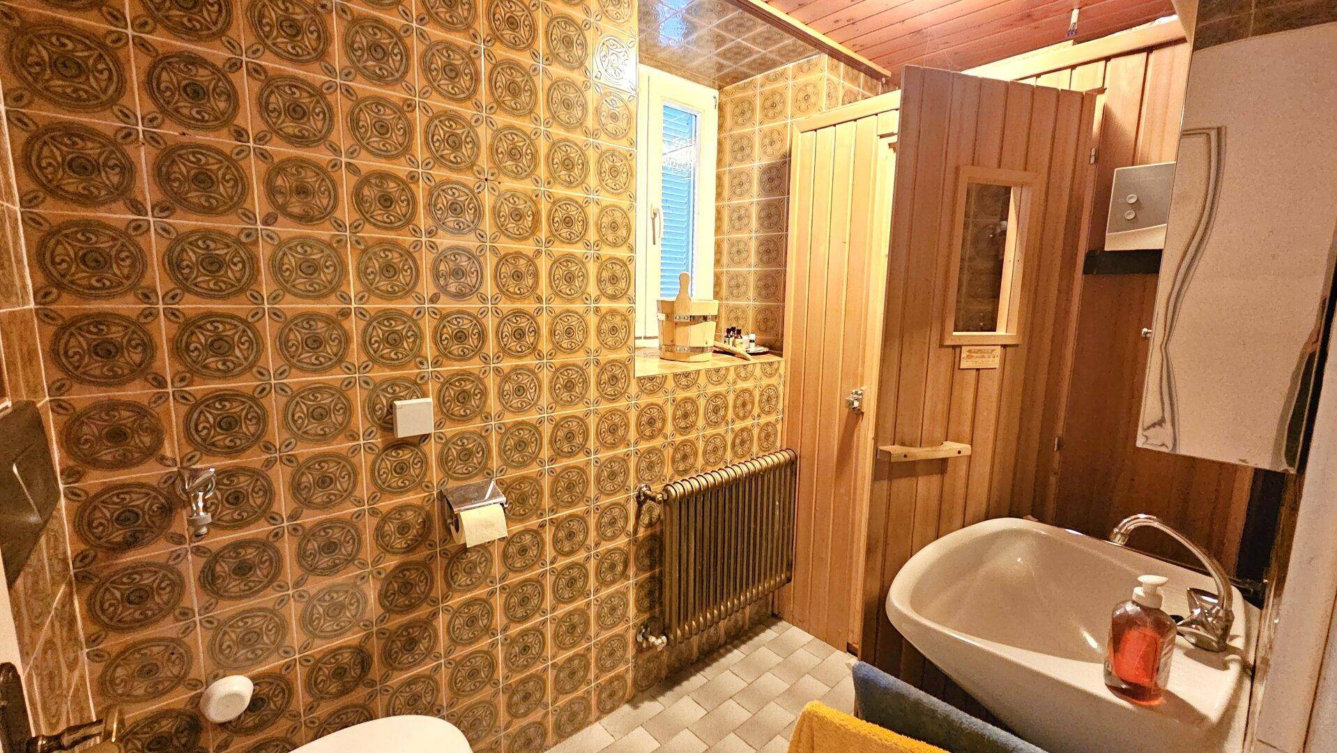 Badezimmer im 80er-Jahre-Stil mit gemusterten Fliesen, Badewanne und integrierter Sauna für Wellness.