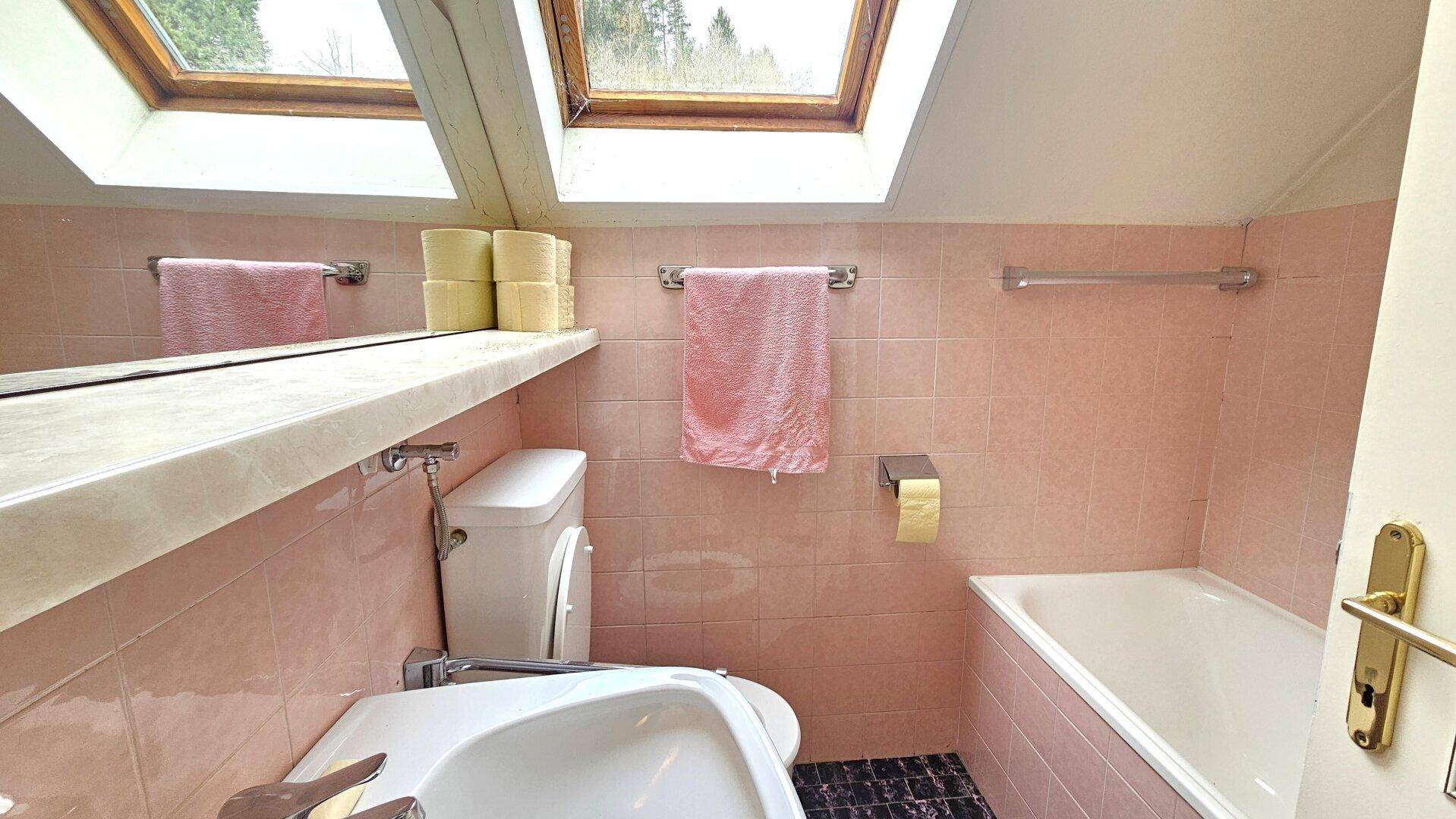 Badezimmer im Dachgeschoss mit rosa Fliesen, Badewanne und Dachfenstern für natürliches Licht.