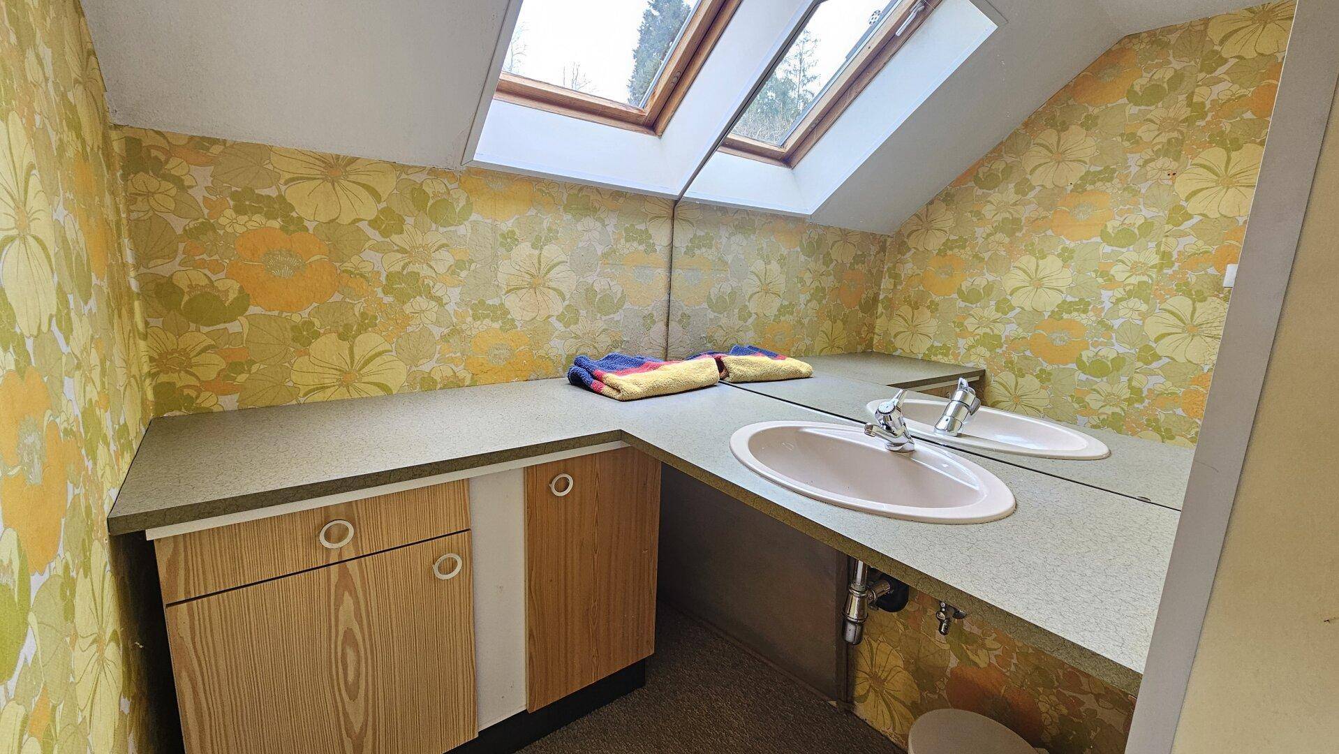 Badezimmer mit floraler Tapete, Doppelwaschbecken und Dachfenstern, die viel Licht hereinlassen.
